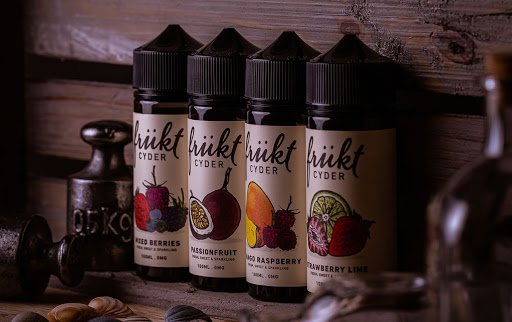 Four bottles of Frukt Cyder Vape Juice against a dark rustic wooden slats. Flavours are mixed berries, passionfruit, mango raspberry and strawberry lime.