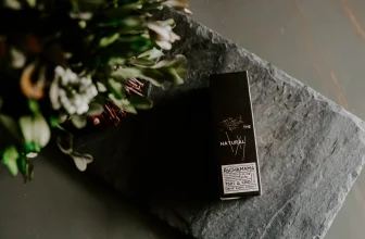 Nicotine salt packaging placed on a smooth, rectangular piece of grey stone with a bunch of flowers in the corner placed in the foreground.