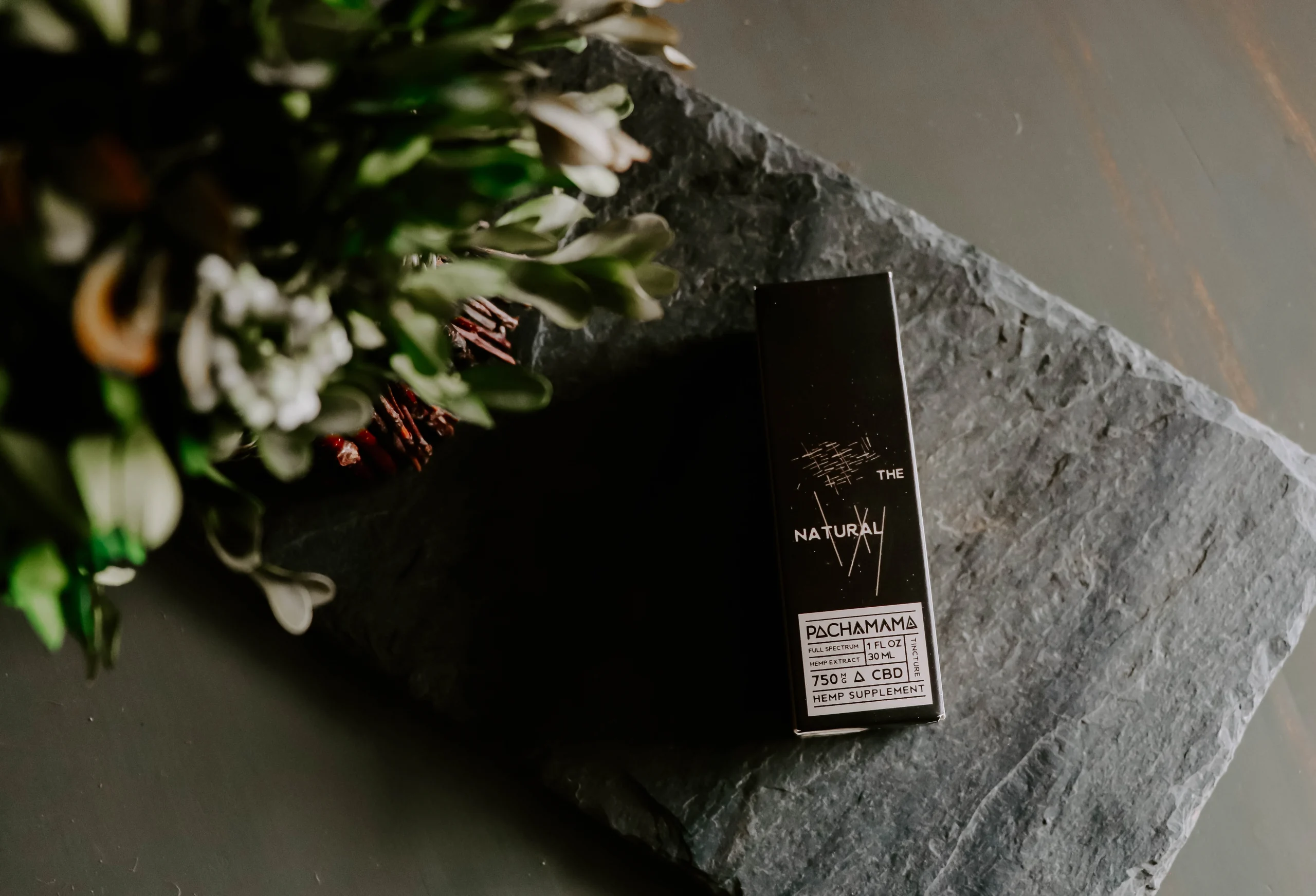 Nicotine salt packaging placed on a smooth, rectangular piece of grey stone with a bunch of flowers in the corner placed in the foreground.